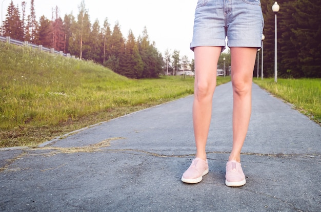 Photo women's slim legs in blue denim shorts and pink sneakers on the sidewalk.