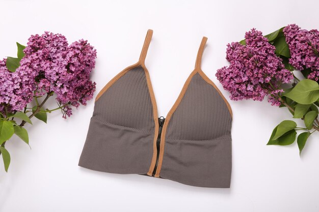 Women's sports bra with branches of blooming lilacs on white background Spring fashion concept Top view Flat lay