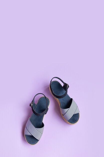 Women's summer striped blue sandals on lilac background with copy space. View from above. Vertical photo