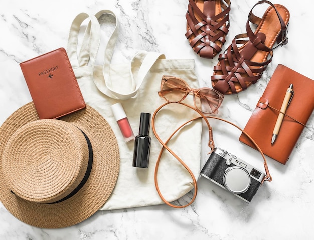 Women's travel accessories textile shopper hat camera passport sunglasses comfortable sandals on a light background top view