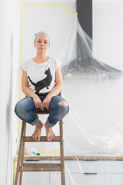 The women sit on a ladder in the kitchen rest during the\
renovation of the apartment eat an apple