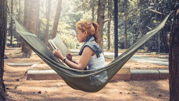 読書に座っている女性。ハンモックで。公園の自然の中で