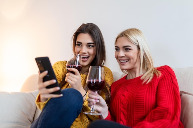 Women sitting on sofa laughing in a cozy loft apartment with\
wine two female friends relaxing on sofa at home with glass of wine\
talking together