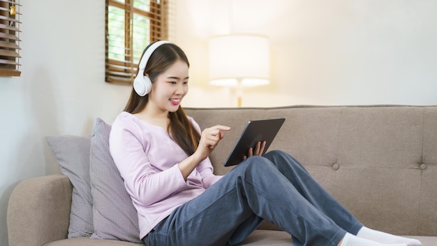 Women sitting on sofa and wearing headphone to using tablet for entertainment in lifestyle at home