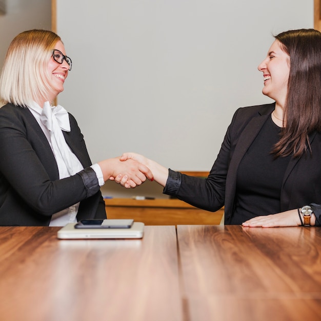 Foto donne sedute al tavolo stringendo la mano sorridente