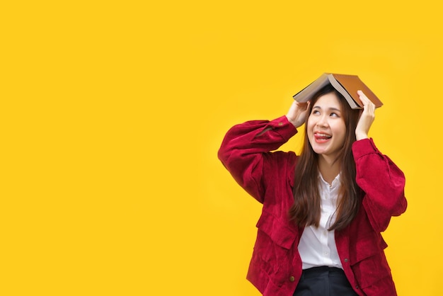 Women smiling and putting book on top of her head with empty space on isolated yellow background