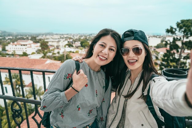 women smiling and taking selfies joyfully on the balcony of an old beautiful house.