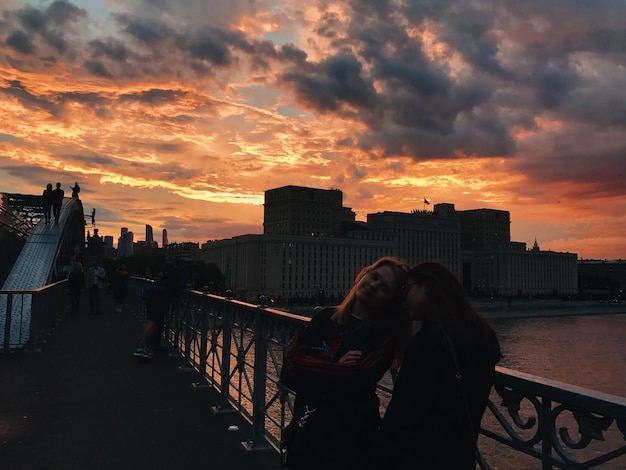 Foto donne in piedi vicino alla ringhiera in città contro il cielo durante il tramonto