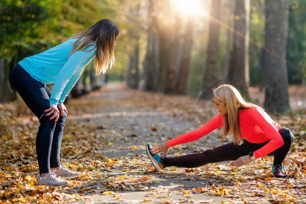 Women stretching with personal fitness trainer after training in the park