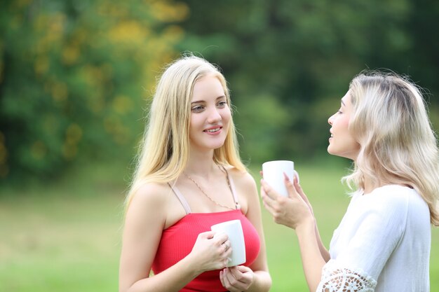 women talking in park with cop of coffee, friendship concept