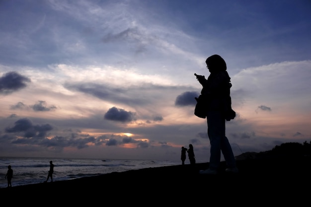日没時にビーチでスマートフォンを使用してテキストメッセージを送信する女性