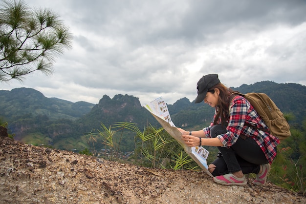 バックパッカーチェックの女性旅行者は、荒野地域の道順を見つけるために地図を作成します