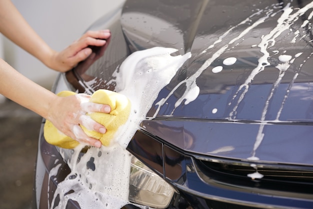 Women washing a soapy grey car with a yellow sponge.