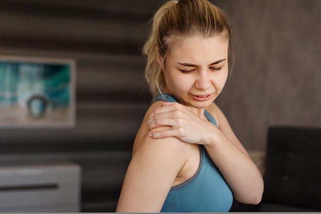 Photo women wearing athletic suits feeling shoulder pain after exercise at home. the danger of self-training