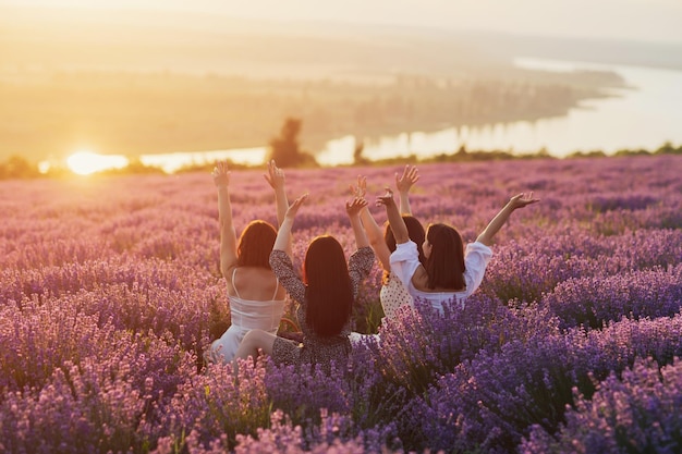 women with hands up sitting in lavender field at sunset