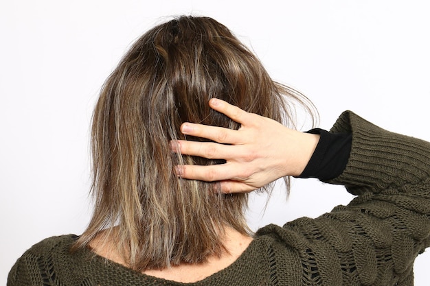 Women with short brown hair in sweater from behind over white background Women with right hand raised onto hair rear view