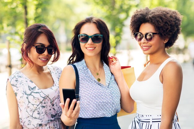 women with smartphones and shopping bags in city