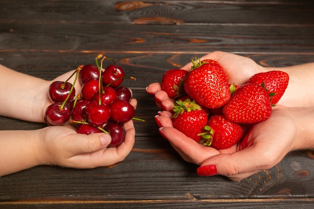 Womens and childrens hands hold fresh berries Cherries and strawberries