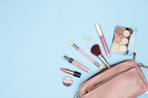 Womens handbag with cosmetics, makeup tools and accessories on a blue background, beauty, fashion, shopping concept, flat lay. High quality photo