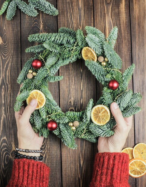 Le mani delle donne decorano una ghirlanda di natale su un tavolo di legno flat lay