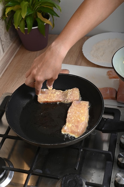 Фото Женские руки жарят кусочки рыбы в кляре из муки и яиц.