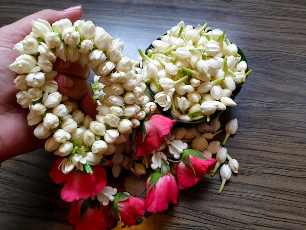 Womens hands hold the thai style of jasmine garland and fresh\
jasmine flowers on wooden background