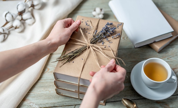 Womens hands is carefully decorating a stack of books with craft paper covers with rope and lavender flowers
