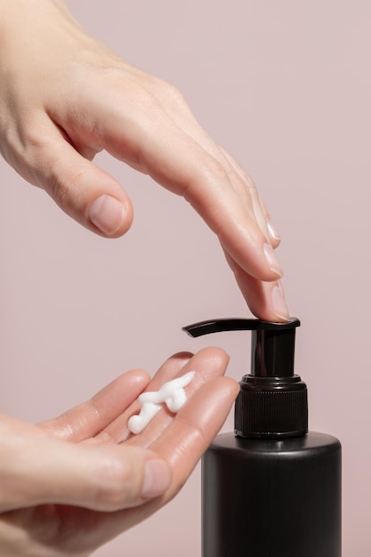 Womens hands press on a black dispenser with a cream