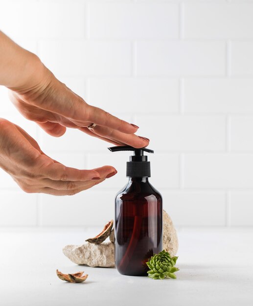 Womens hands press on a glass brown dispenser with liquid soap or gel