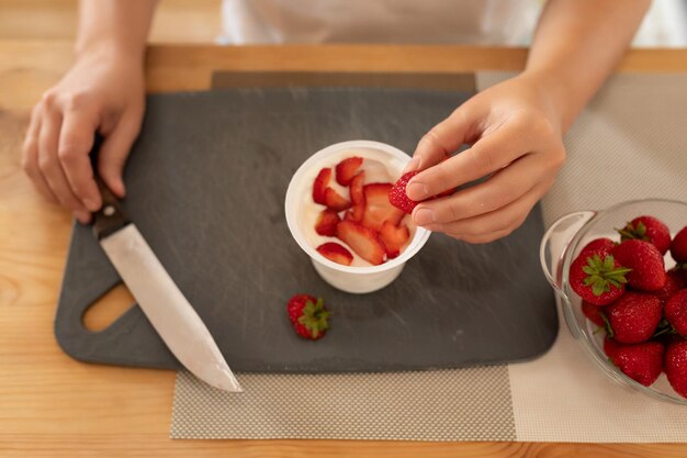 Photo womens hands put strawberries in a jar of sour cream