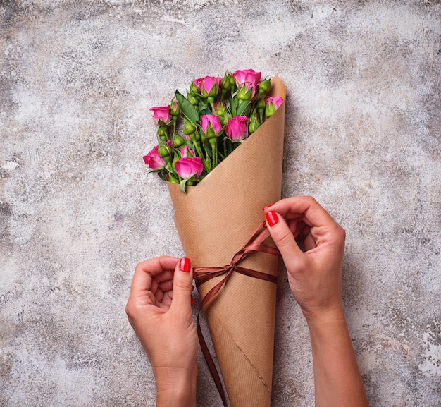 Womens hands wrap a bouquet of roses in paper