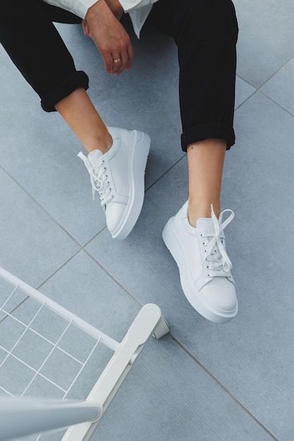 Womens legs in black trousers and white leather sneakers Modern casual style New shoe collection