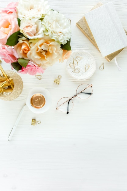 Photo womens workspace with pink and beige roses flowers bouquet accessories diary glasses on white