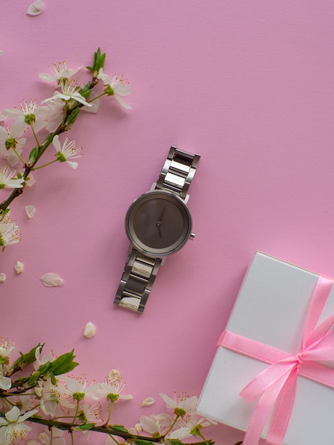 Womens wristwatch on pink background with cherry flowers and copy space