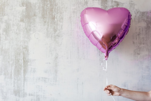 wonan's hand holding a pink heart balloon on gray concrete background copy space