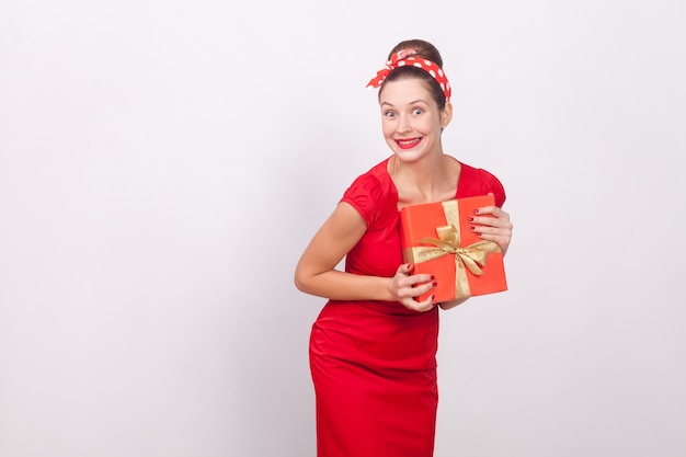 Wonder and happy woman holding gift box. Indoor, studio shot, isolated on gray background