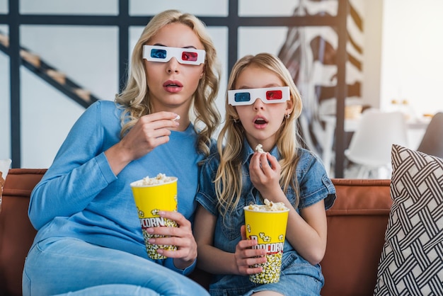 Чудо-мать с милой маленькой дочерью в 3D-очках на диване и едят попкорн