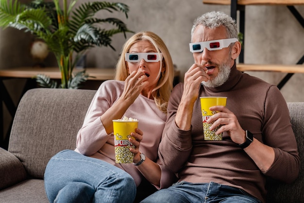 Wonder van middelbare leeftijd paar in 3D-bril met popcorn kijken naar film op de bank