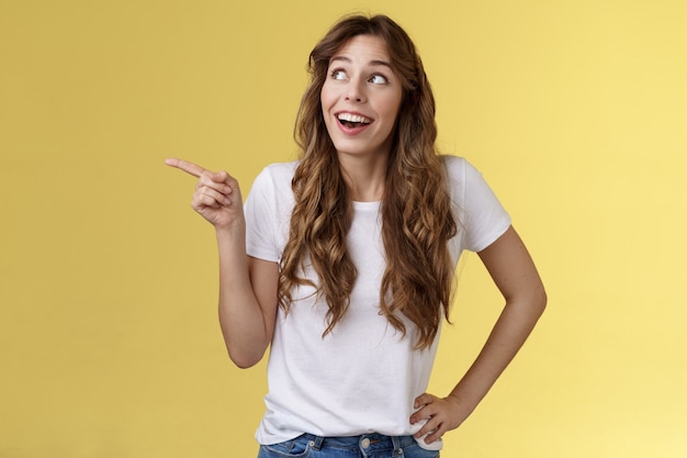 Chiedo impressionato carismatico affascinato sorridente felice ragazza indicando sguardo in alto a sinistra senza parole sorpreso sogghignando a trentadue denti felicità gioia espressione contemplare grande vista sfondo giallo