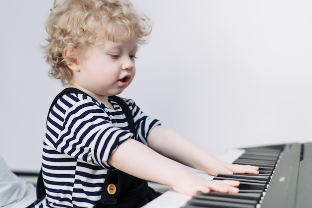 Wonderful baby boy in cute clothes learns to play the piano