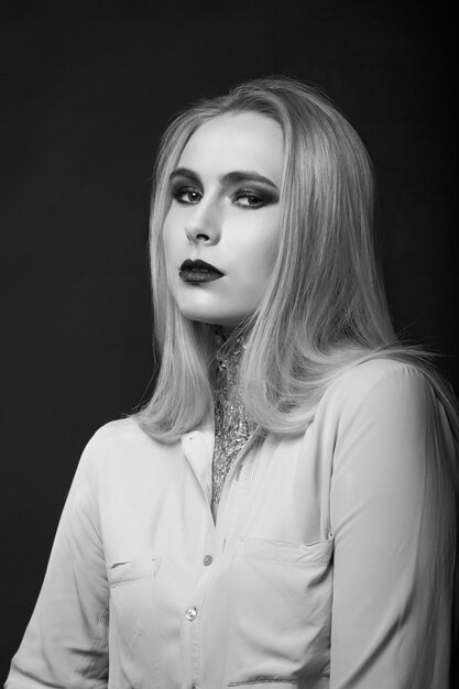 Wonderful blond model posing at studio with bright makeup and foil on her neck. Monochrome shot