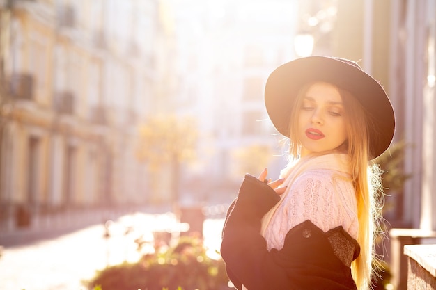 Wonderful blonde woman wearing sweater and hat posing at the old street. Space for text