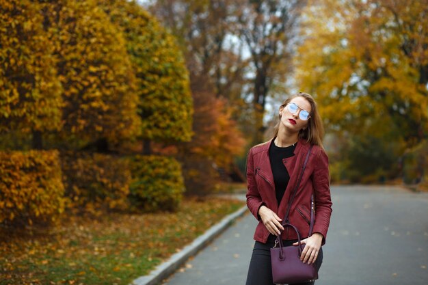 Wonderful blonde woman with red lips wearing leather jacket, purse and red glasses. Space for text