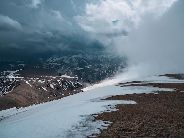 Wonderful dramatic landscape with big snowy mountain peaks above low clouds. Snow storm on top of a mountain. Atmospheric large snow mountain tops in cloudy sky.