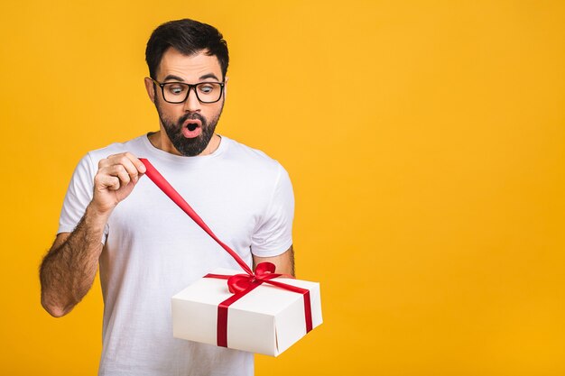 Wonderful gift! Adorable photo of attractive bearded man with beautiful smile holding birthday present box isolated over yellow background.