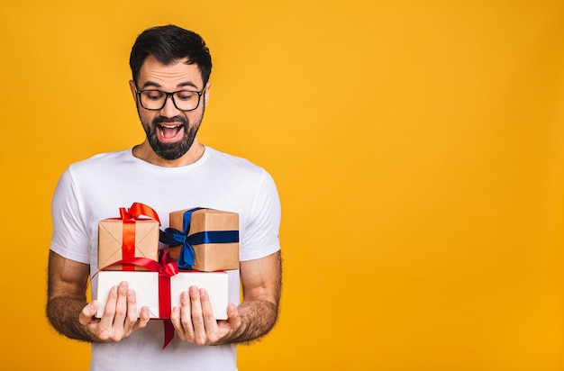 Wonderful gifts! Adorable photo of attractive bearded man with beautiful smile holding birthday present boxes isolated over yellow background.