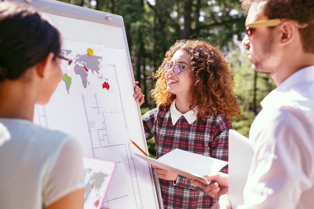 Wonderful idea. Cheerful curly-haired girl presenting her project and her friends listening to her