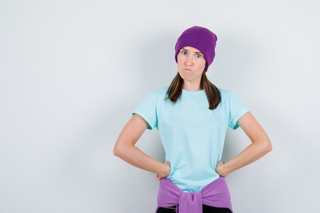 Wonderful lady with hands on waist in blouse, beanie and looking furious , front view.