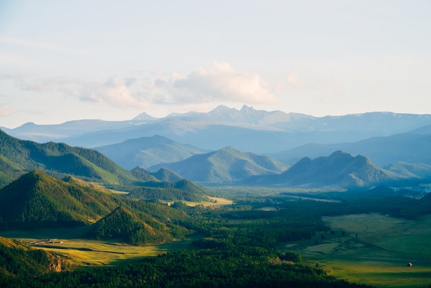 Wonderful mountain land with forest and small houses in sunlight. Scenic view to vast expanses of rolling hills and great mountain ridge on horizon. Immense distances of wavy relief in evening light.