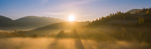 멋진 산 풍경입니다. 가을 Carpathians의 새벽, 안개와 노란 가을 나무에 빛나는 태양 광선. 드론보기.